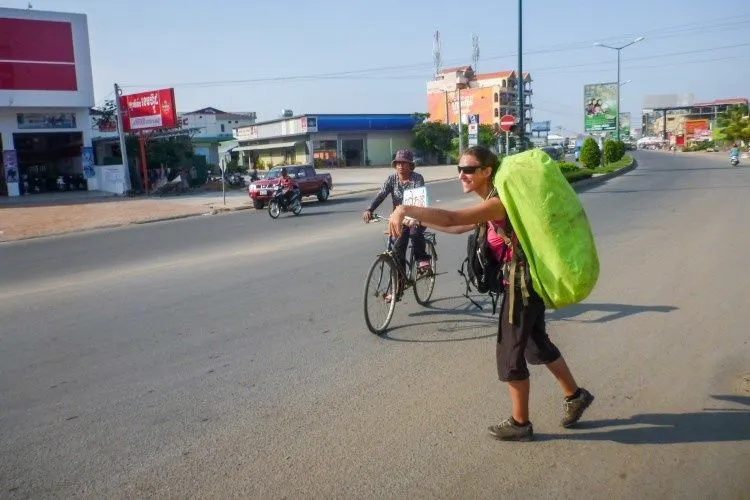 Jenni, sac à dos sur le dos, fait du stop au bord d'une avenue cambodgienne