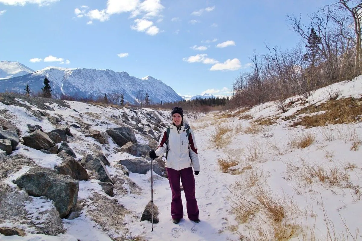 Jenni, bâtons en main, sur le début du sentier enneigé de Sam McGee avec des montagnes en fond