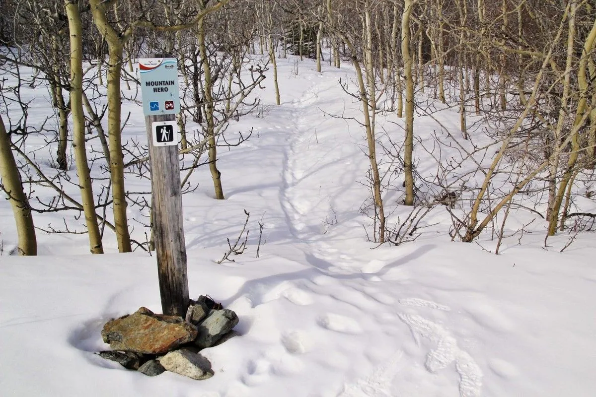 Panneau Mountain Hero planté dans un tas de pierres, au départ d'un sentier de randonnée enneigé