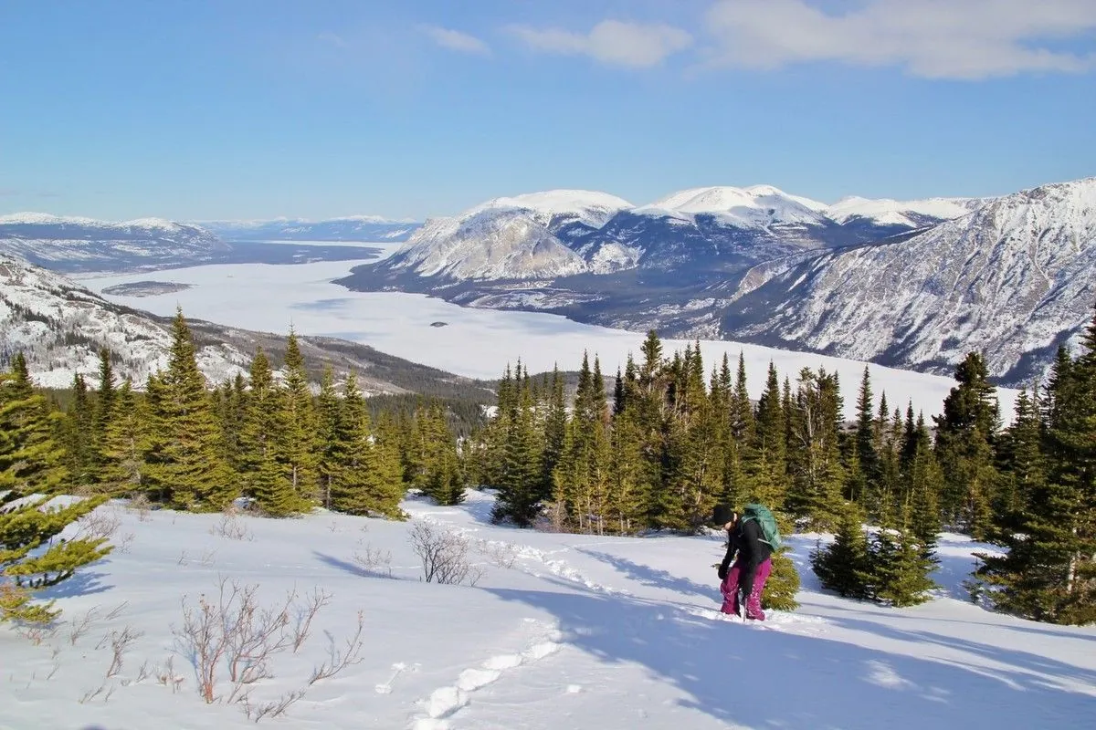 Une randonneuse progresse dans la neige profonde, avec en toile de fond le lac gelé et les montagnes