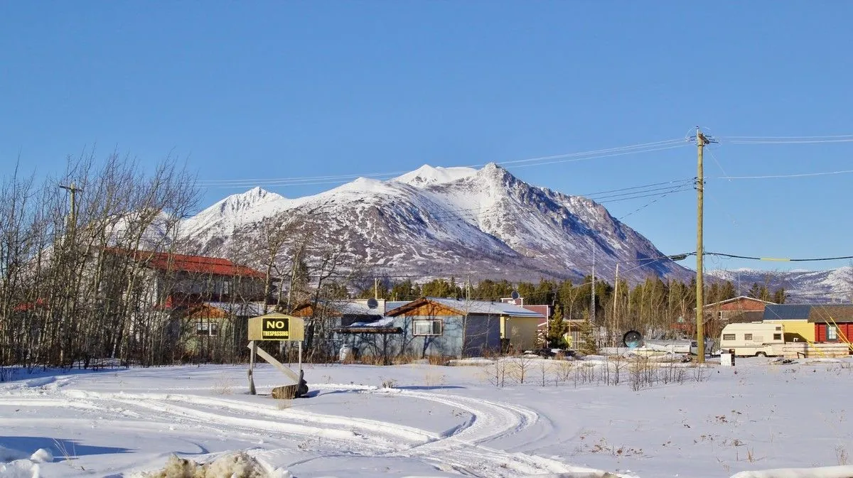 Rue enneigée du village de Carcross, avec ses maisons basses et une montagne blanche au fond