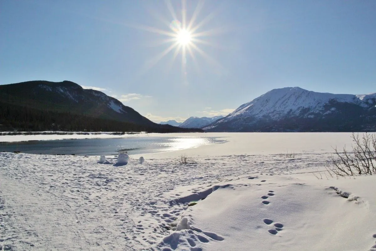Soleil en étoile au-dessus du lac Bennett qui commence à dégeler, entouré de montagnes