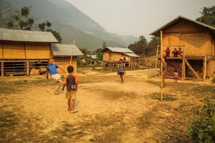 Enfants jouant au ballon entre les maisons en bambou sur pilotis d'un village voisin de Muang Ngoi