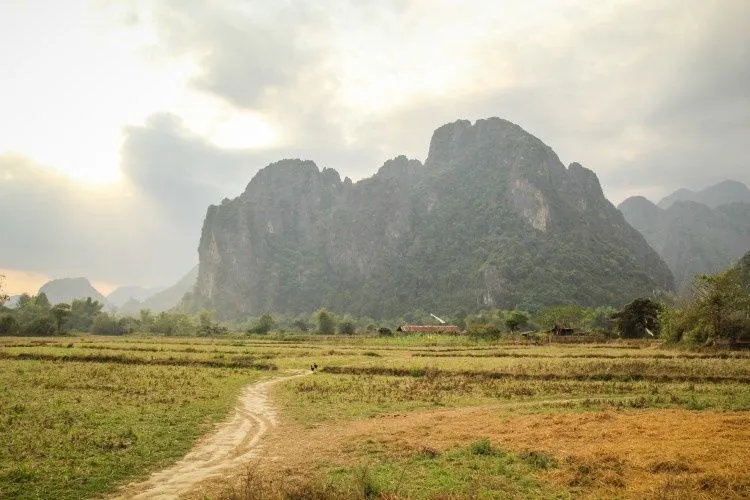 Piton calcaire dominant les rizières sèches et un chemin de terre près de Vang Vieng