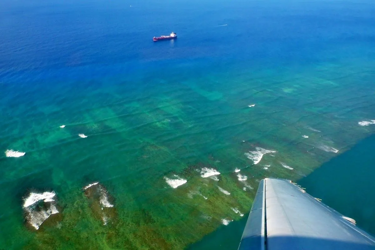 Eau turquoise et récifs vus du hublot de l'avion lors du vol vers Kaua'i, avec un cargo au large