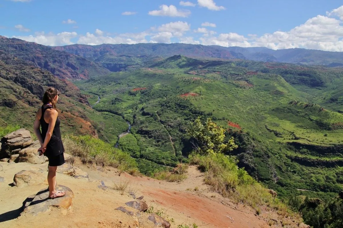 Une randonneuse contemple le canyon de Waimea, vallée verte et falaises rouges, à Kaua'i