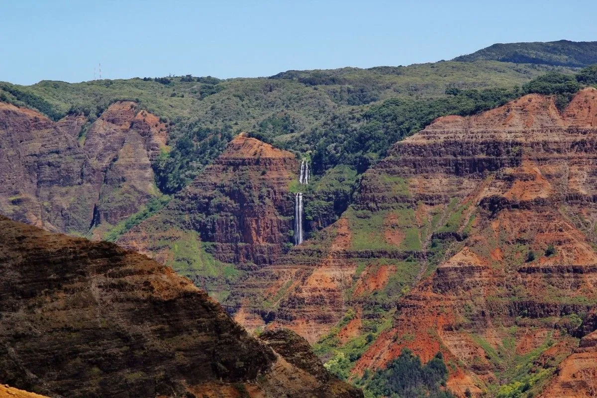 Cascade qui tombe entre les strates rouges des parois du canyon de Waimea, à Kaua'i