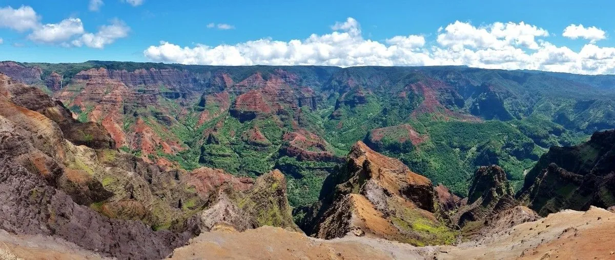 Panorama du canyon de Waimea aux reliefs déchiquetés rouges et verts sous un ciel nuageux