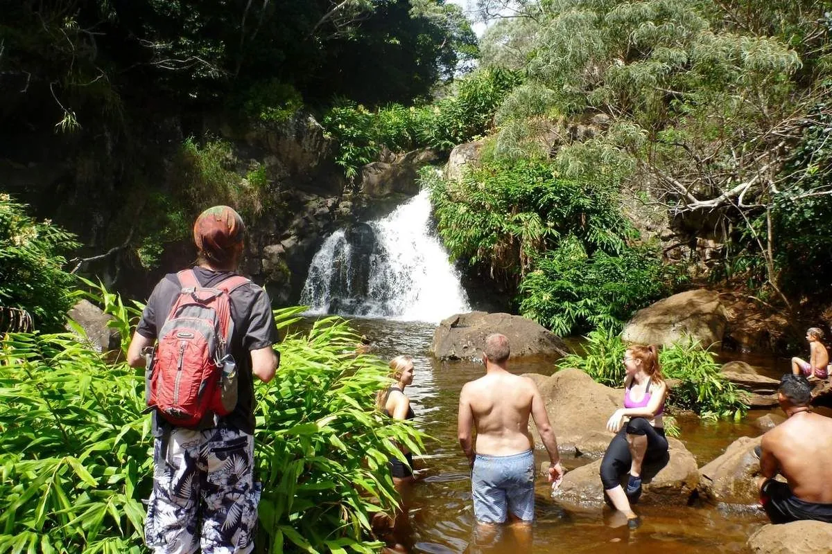 Un randonneur observe la cascade, tandis que des baigneurs se rafraîchissent dans le bassin naturel